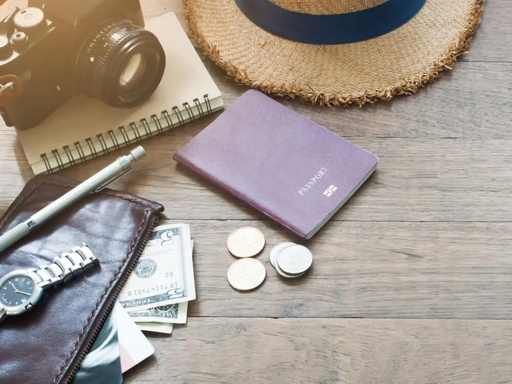 Travel essentials laid out on a wooden table, including a passport, wallet with cash, and a camera, representing the process of planning a budget for a trip to Bali.