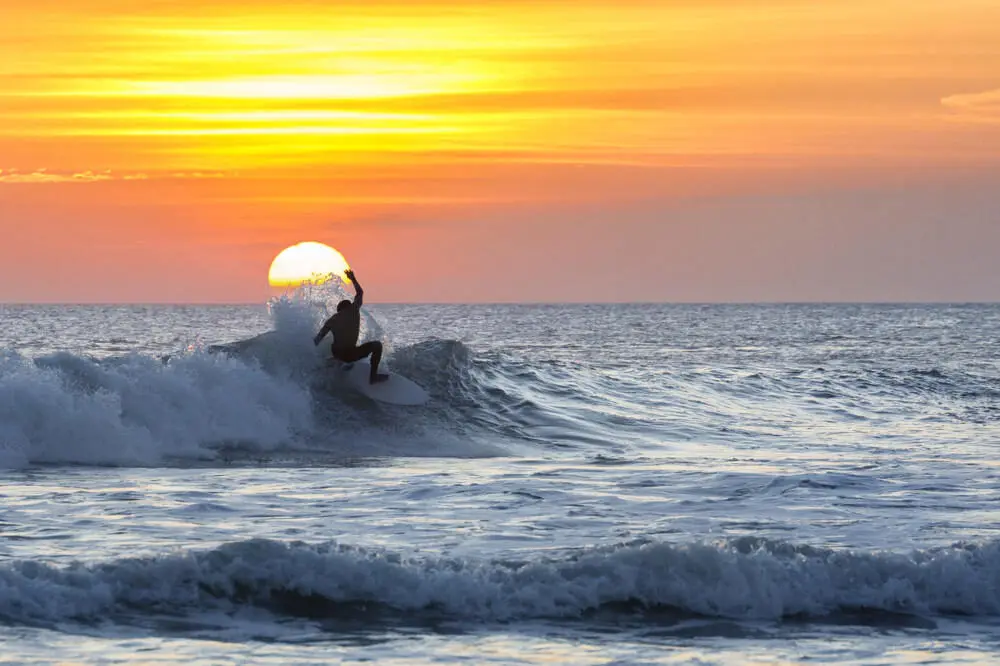 A surfer silhouetted against a vibrant golden sunset while riding a wave at Kuta Beach in Bali.