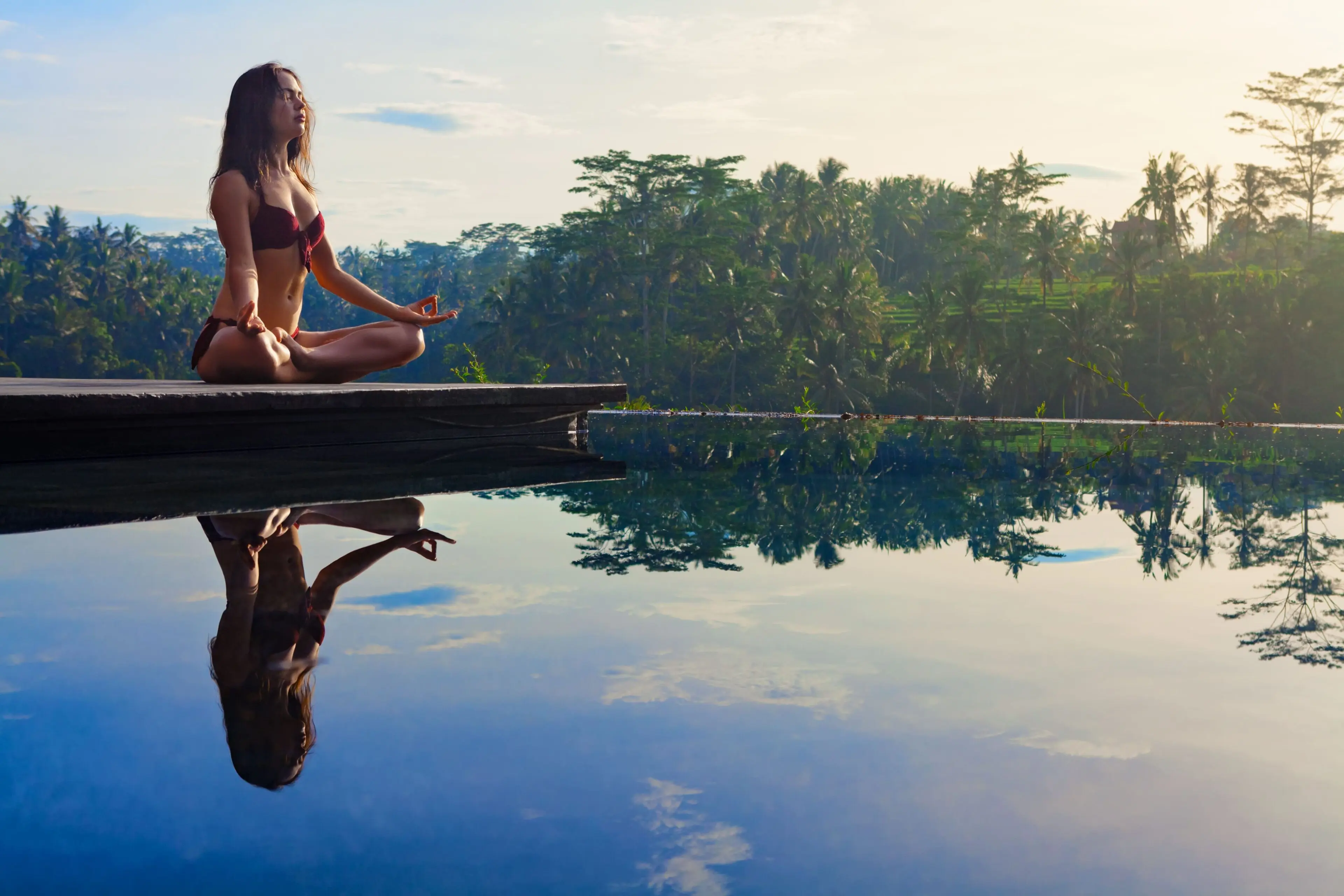 Woman meditating by an infinity pool in Ubud surrounded by tropical jungle, representing a Bali wellness itinerary
