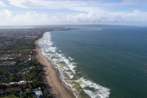 An aerial shot of the long, sandy beach and gentle waves of Legian and Double Six, with hotels and buildings lining the coast.