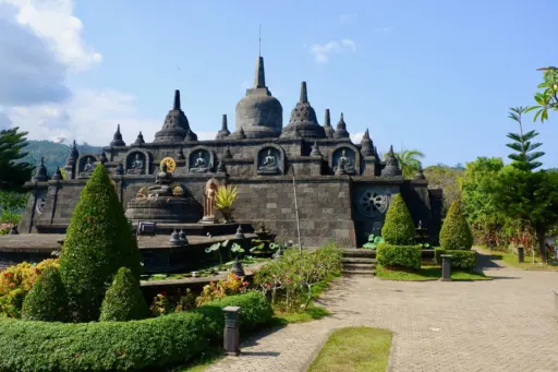 The main building of Brahmavihara-Arama, a Buddhist monastery in North Bali, with a tiered structure and statues, surrounded by serene gardens and a clear blue sky.