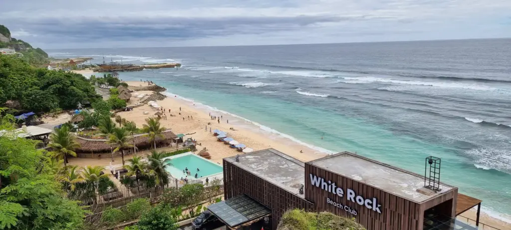 View of Melasti Beach Bali with turquoise waves, white sand, and the White Rock Beach Club on the Bukit Peninsula coastline