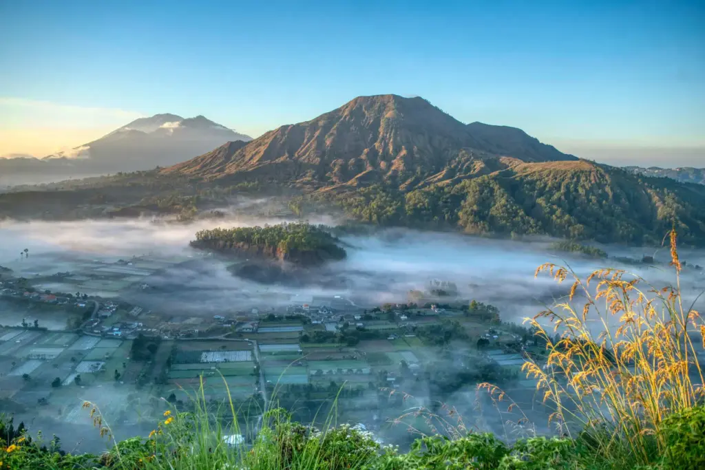 Mount Batur at sunrise with misty valleys and farmlands, a highlight of Bali mountains and volcano hikes