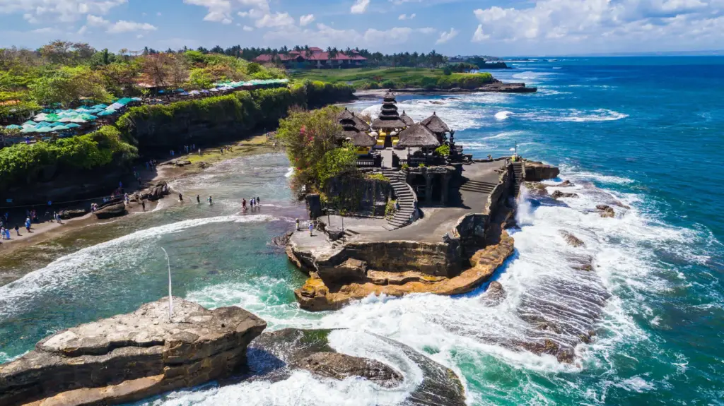 Tanah Lot Bali sea temple on a rocky outcrop with ocean waves and visitors exploring the coast