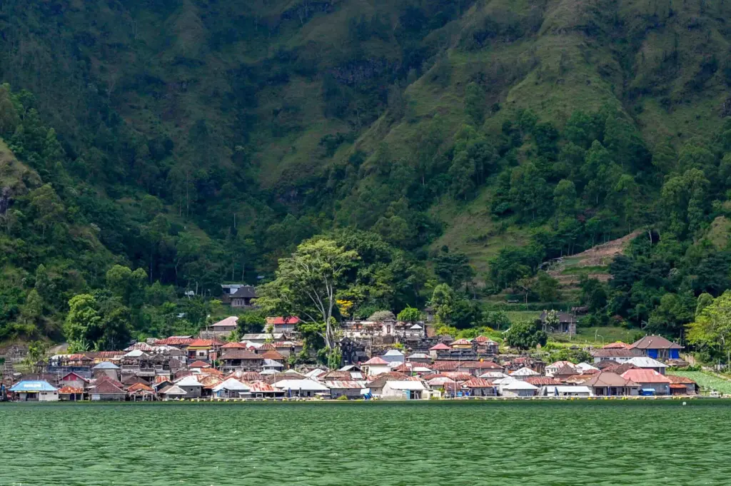 Trunyan Village Bali on the shores of Lake Batur, surrounded by lush green hills and traditional houses.