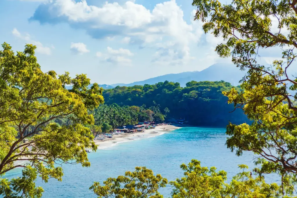 View of Pasir Putih Bali, also known as Virgin Beach, with white sand, turquoise water, and green hills in East Bali.